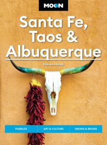 Book jacket featuring image of cow skull and chiles hanging on a stucco wall with text Moon Santa Fe, Taos & Albuquerque